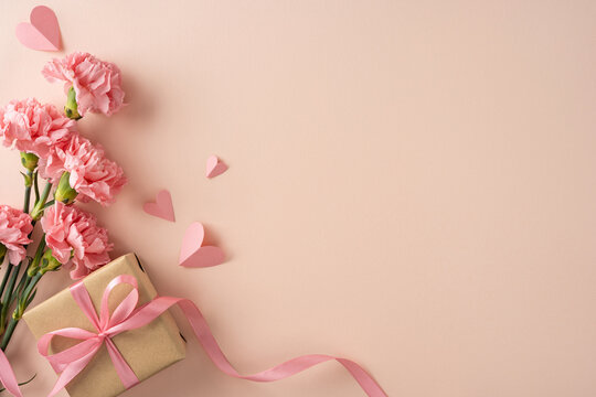 Happy Mother's Day arrangement featuring pink carnations and a kraft-wrapped gift tied with pink ribbon and scattered paper hearts ideal for greeting cards and social posts