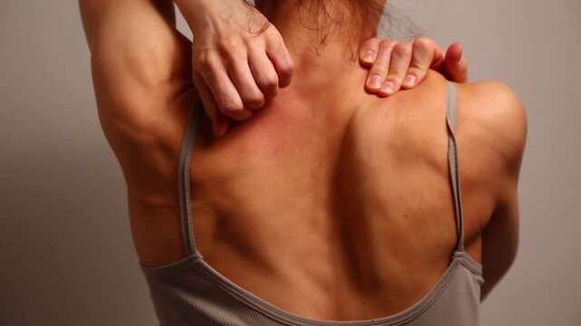 Health sport body woman doing massage with hands her neck, shoulders, upper back. Fit naked muscles model in bra isolated in studio light with copy space. Back view closeup