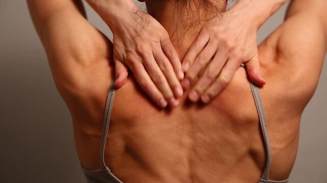 Health sport body woman doing massage with hands her neck, shoulders, upper back. Fit naked muscles model in bra isolated in studio light with copy space. Back view closeup