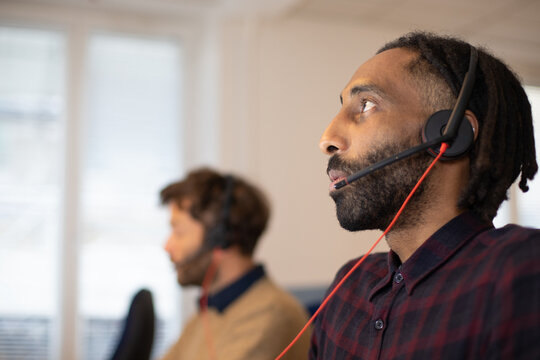 portrait d'un t&eacute;l&eacute; conseiller au travail qui porte un micro-casque.Il est souriant et travaille avec ses coll&egrave;gues