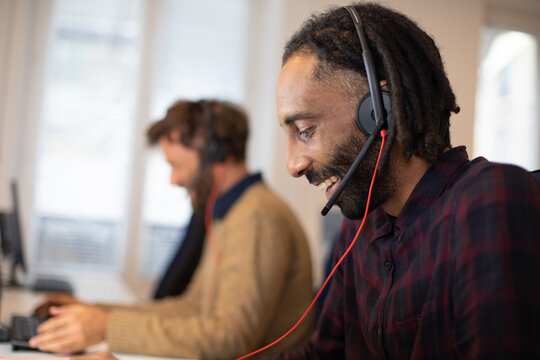 portrait d'un t&eacute;l&eacute; conseiller au travail qui porte un micro-casque.Il est souriant et travaille avec ses coll&egrave;gues