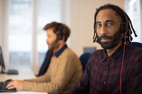 portrait d'un t&eacute;l&eacute; conseiller au travail qui porte un micro-casque.Il est souriant et travaille avec ses coll&egrave;gues