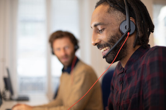 portrait d'un t&eacute;l&eacute; conseiller au travail qui porte un micro-casque.Il est souriant et travaille avec ses coll&egrave;gues