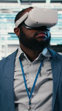 Vertical video Portrait of smiling man in data center putting VR headset on to optimize electronics. Cheerful server hub system administrator using virtual reality simulation to monitor system