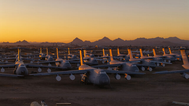 Tucson, United States - 06 February 2025: Aerial view of rows of retired C-5 Galaxy aircraft, their silhouettes stark against the fiery sunset, a silent testament to aviation history.