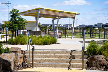 Obraz premium Steps and landscaped transition in a modern suburban park in Manor Lakes, Melbourne, Australia, featuring stone stairs, handrails, and a shaded public seating in background.well-designed outdoor space