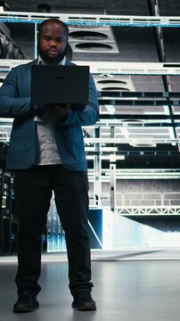 Vertical video Team of server farm software developers using laptop to optimize electronics. Data center teamworking colleagues brainstorming, using notebook to monitor system performance bottlenecks