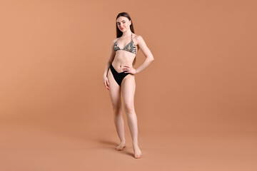Naklejka premium Beautiful young woman wearing stylish bikini on brown background