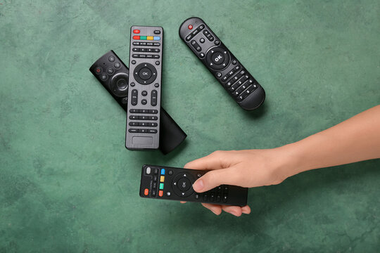 Female hand with different modern TV remote controls on green grunge background
