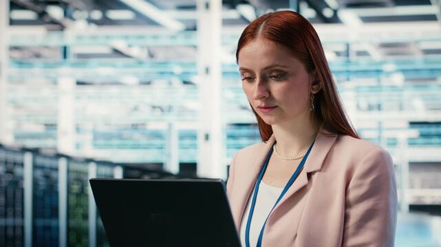 Happy woman in server room using notebook to enhance operational effectiveness of infrastructure. Joyous female engineer in data center using laptop to monitor rigs metrics, camera B