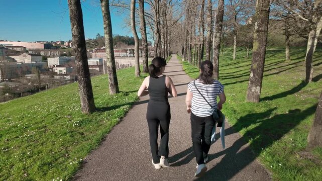 Back view of two female friends enjoying a relaxing walk together on a path in a public park, embracing a healthy lifestyle and the practice of mindfulness on a bright day