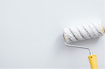 Obraz premium Paint roller with yellow handle rests against a plain white wall.