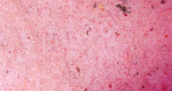 Abstract background of pink and golden glitter scattered over white liquid paint, creating a bright sparkling texture for festive design and creative projects. Slow motion.