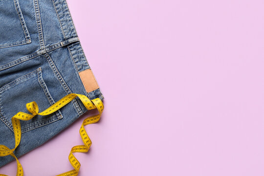 Jeans with measuring tape on purple background. Anorexia concept