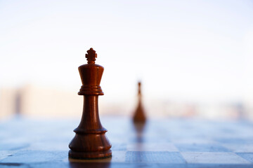A cinematic contemplative shot captures two chess pieces silhouetted against a bright, hazy cityscape background. The selective focus highlights one piece in a strategic face-off, symbolizing competit © kareem