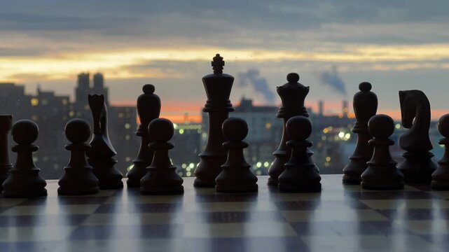 A dramatic low-angle shot captures chess pieces in silhouette against a vibrant sunrise sky and a reflective surface. The image evokes themes of strategy, planning, and challenge, perfect for business