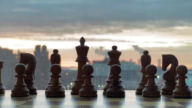 A dramatic low-angle shot captures chess pieces in silhouette against a vibrant sunrise sky and a reflective surface. The image evokes themes of strategy, planning, and challenge, perfect for business