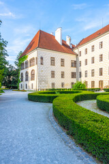 Fototapeta premium Trebon Castle stands in the background while visitors walk along the path. The garden is well kept with trimmed bushes. Sunlight shines on the stone walls.