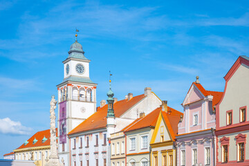 Fototapeta premium The lookout tower stands tall in Trebon. The colorful buildings surround it under a clear blue sky. People enjoy the view and the space around the tower during a sunny day.