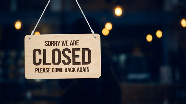 Wooden sign displaying Sorry We Are CLOSED Please Come Back Again hanging on a glass door with warm bokeh lights in the background