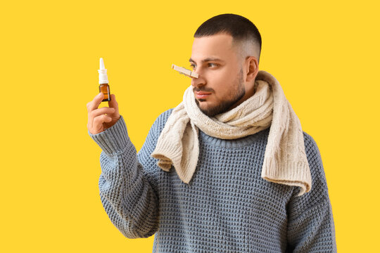 Ill young man with clothespin and nasal drops on yellow background. Stuffy nose concept