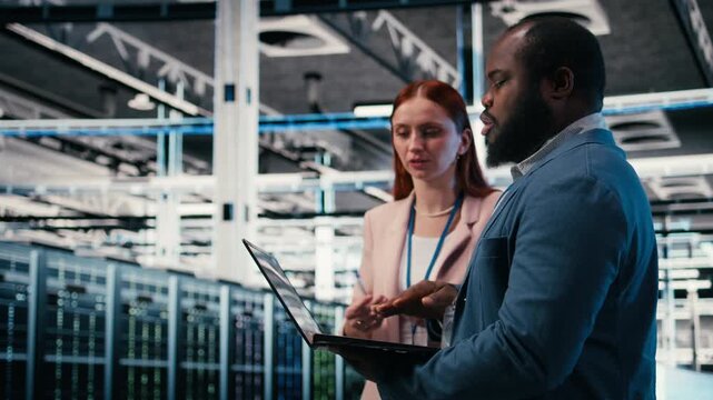 Engineering team solving tasks in server farm using laptop, doing network management virtualization. Teamworking data center colleagues oversee IT infrastructure supercomputers with notebook, camera A