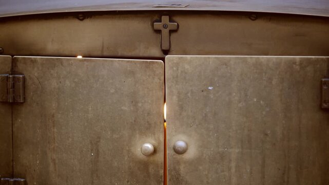 A candle burns softly, casting warm light through the gap of heavy metal doors
