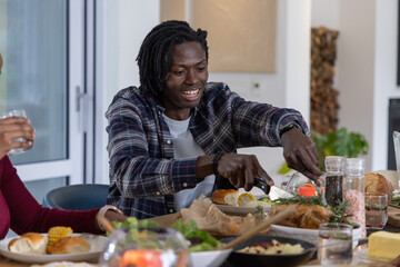 Diverse couple sitting at dining table, African American adult male carving roast with knife fork © wavebreak3