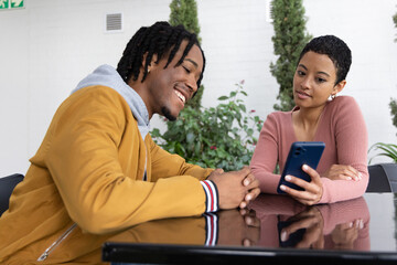 Fototapeta premium Diverse friends sharing blue phone at shared lounge black table, man jacket, woman ribbed top
