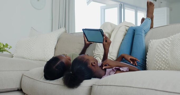 Holding tablet above them, two children wearing jeans watching tablet in living room for sharing