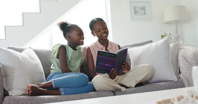 Older sister opening book, reading aloud on sofa, younger sister leaning in, bonding education