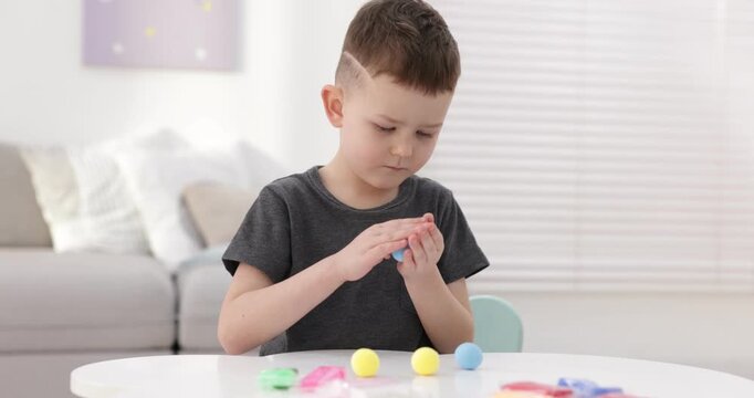 Little boy sculpting with play dough at white table indoors