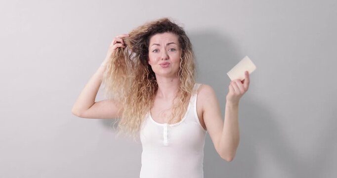 Unhappy woman trying to brush her tangled hair on light grey background