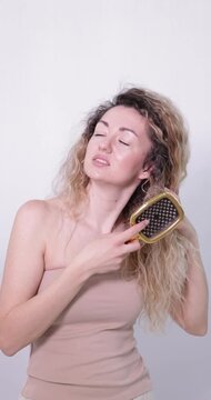 Unhappy woman trying to brush her tangled hair on light grey background