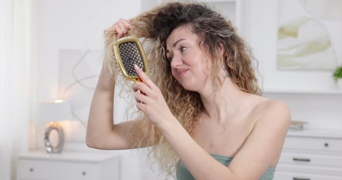Unhappy woman trying to brush her tangled hair at home