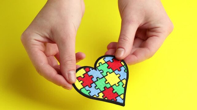 Autism. Woman with heart made of puzzle pieces on yellow background, closeup