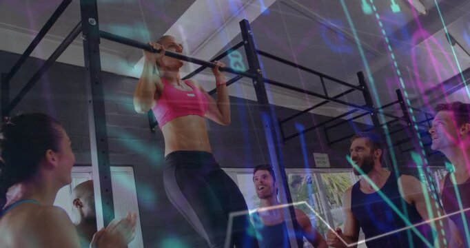 Adult woman gripping pull-up bar, pulling chin above bar, doing reps in gym while peers cheering