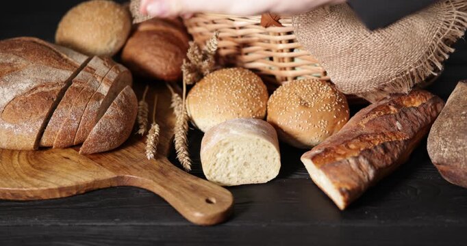 Woman taking piece of bread at black wooden table, closeup