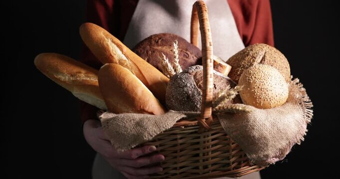 Woman with different types of bread loaves in wicker basket on black background, closeup