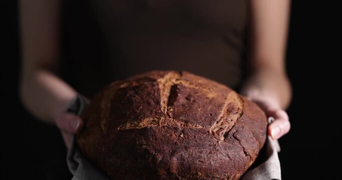 Woman holding loaf of rye bread on black background, closeup