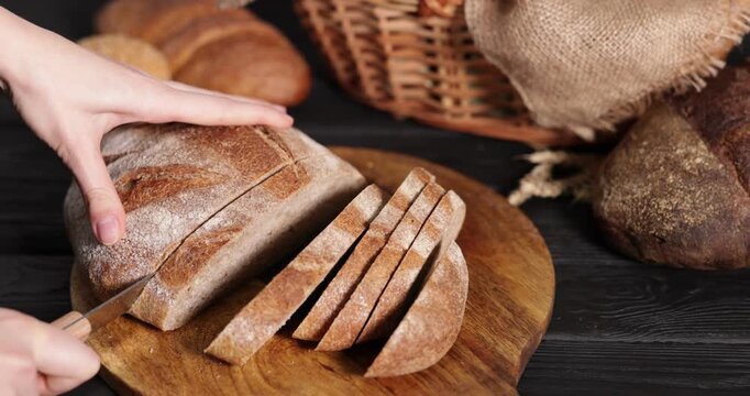 Woman cutting loaf of bread at black wooden table, closeup