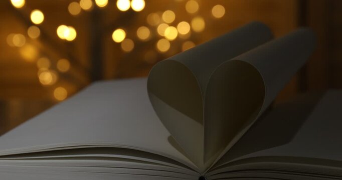 Heart made of book pages on table against blurred lights, closeup. Bokeh effect