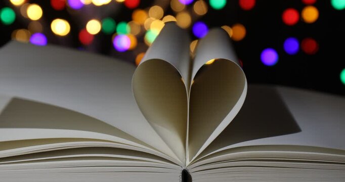 Heart made of book pages on table against blurred lights, closeup. Bokeh effect