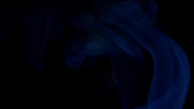 Abstract footage of flowing blue smoke drifting gracefully against a dark black background, creating a dramatic and cinematic atmospheric effect. The soft swirling vapor patterns