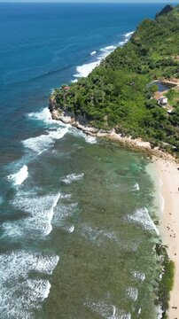 An aerial view of the lush green coastline meeting the clear turquoise waters at Karimun Jawa, Indonesia, featuring rocky formations and dense vegetation, highlighting the natural beauty of this tropi