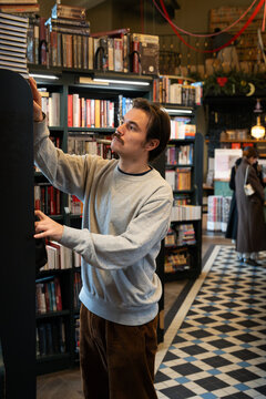 Intelligent focused man booklover searching books and publications from shelf in trendy bookstore. Thoughtful male literature fan visiting bookshop for purchasing popular books and new bestsellers.