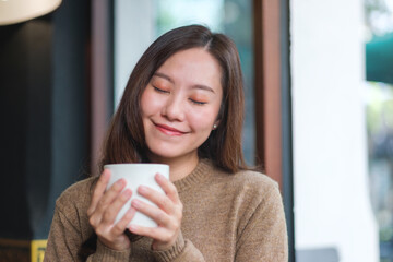 Portrait image of a woman with closed eyes holding and drinking hot coffee