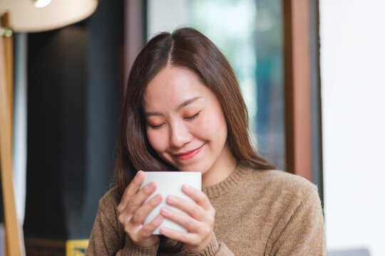Portrait image of a woman with closed eyes holding and drinking hot coffee