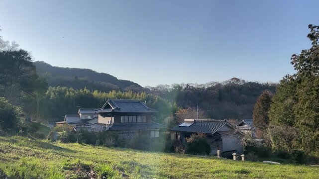 A quiet rural scene in Japan, featuring a narrow path leading through a peaceful village. The atmosphere is calm and timeless, with soft natural light and minimal movement.