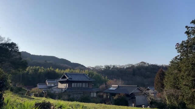 A quiet rural scene in Japan, featuring a narrow path leading through a peaceful village. The atmosphere is calm and timeless, with soft natural light and minimal movement.